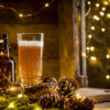 Beer in glass on wooden background with Christmas lights and pine cones. Studio shot
